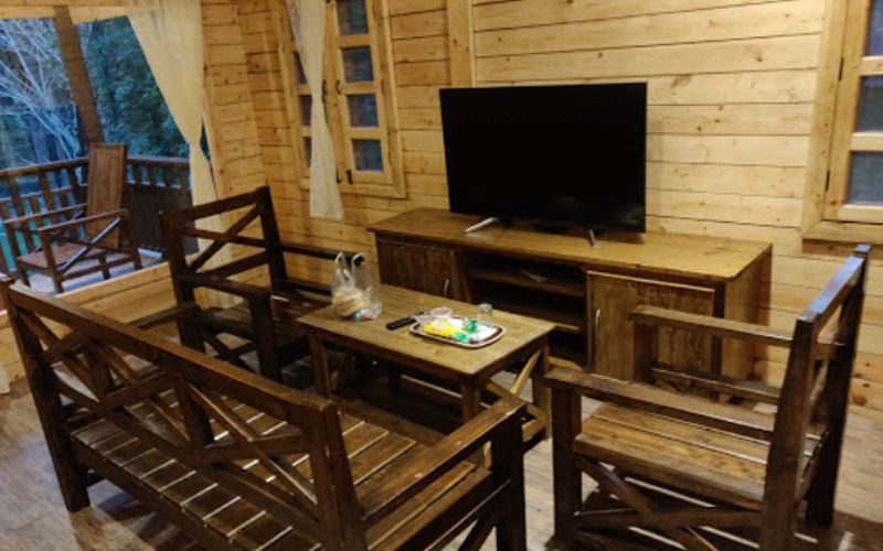 Living room with television and wooden furniture in a cottage at The Woods Resort Maredumilli